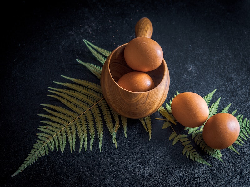 a wooden cup with two brown eggs in it and two others on the side.